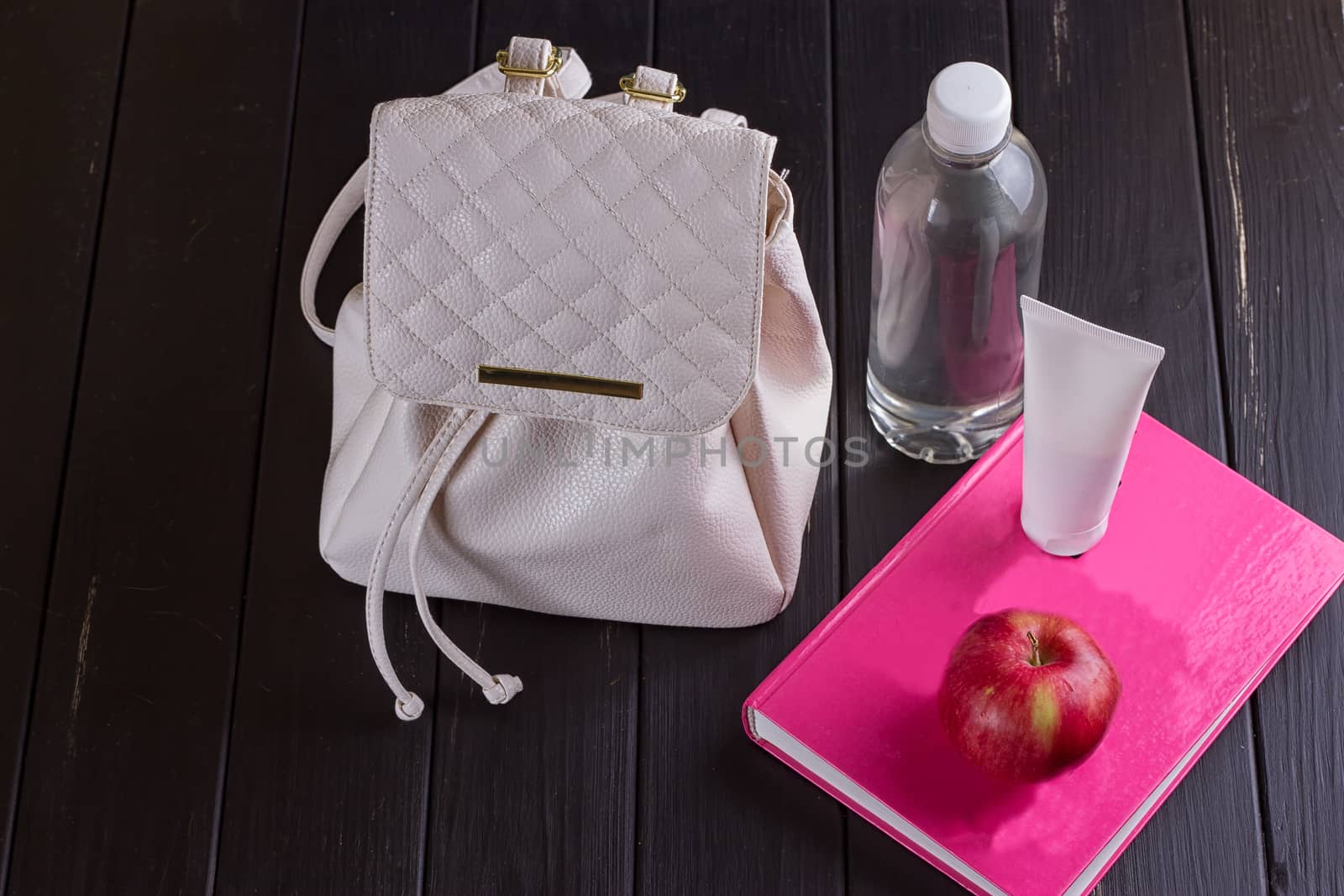 White leather backpack, pink book, bottle of water on a black background