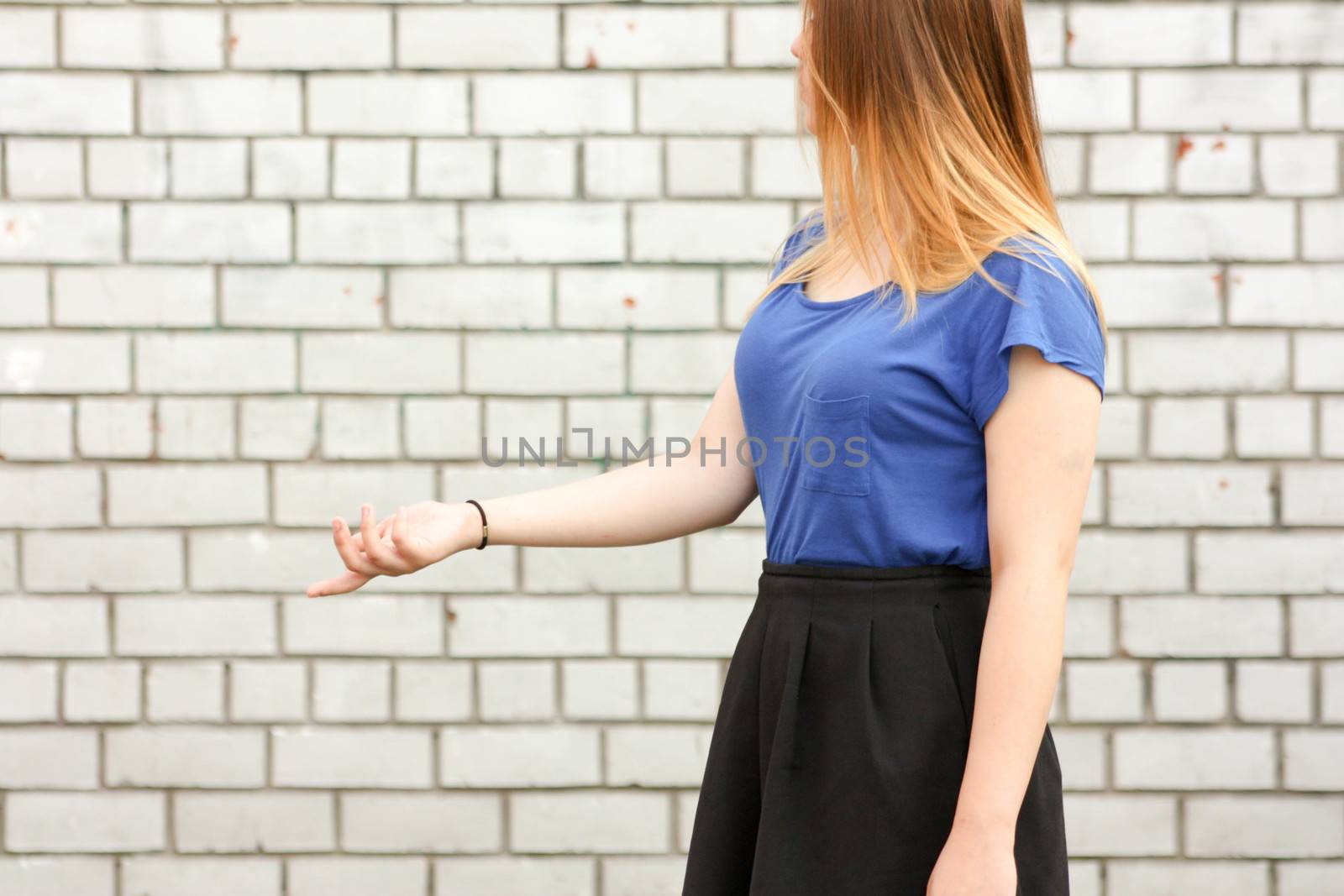 Learning concept. The girl is at the white brick wall. Photo for your design. Holds his hand with his open palm forward in profile