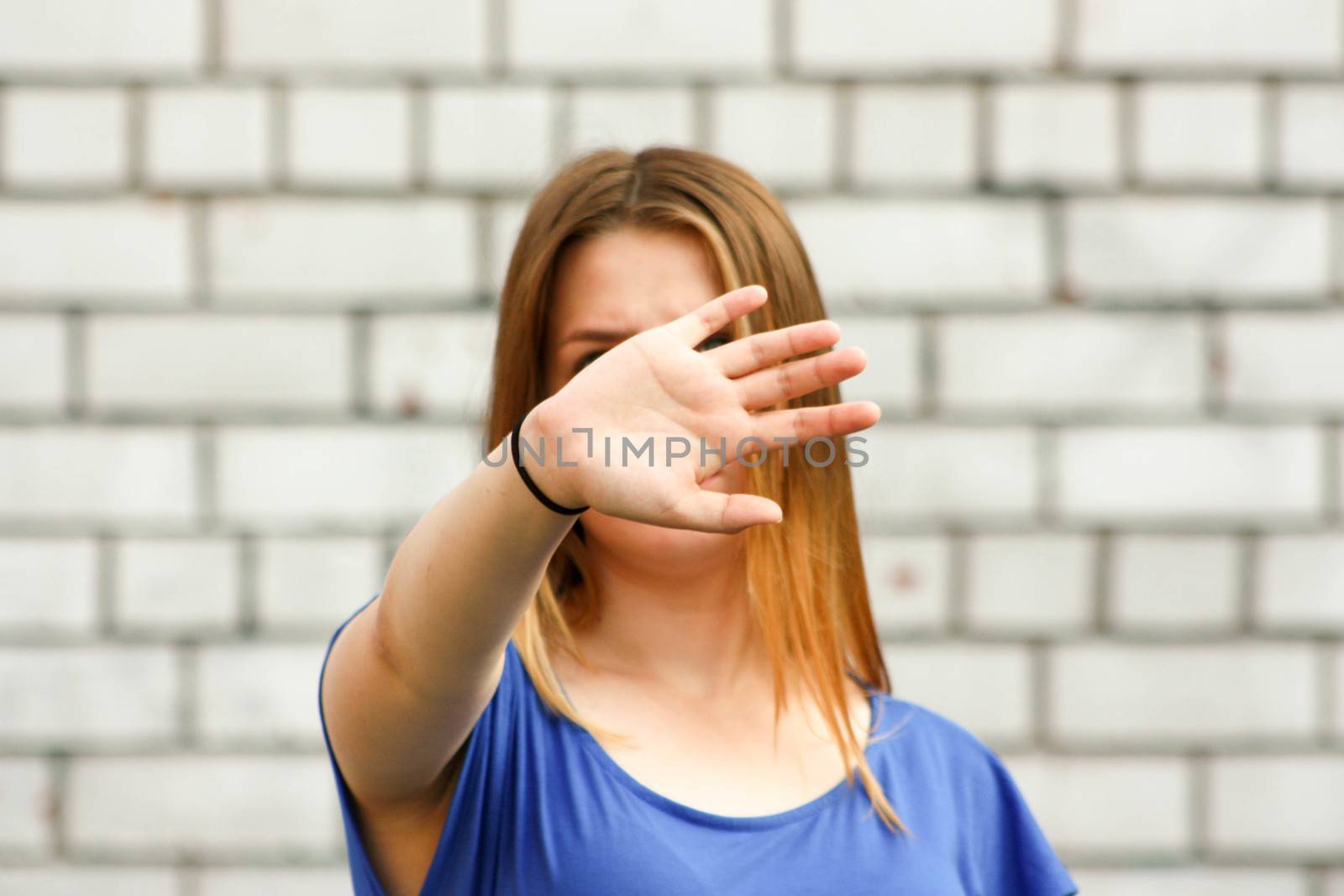 Learning concept. The girl is at the white brick wall. Photo for your design. Holds his hand with the palm of his hand. Prohibition, unwillingness to learn. Teenager