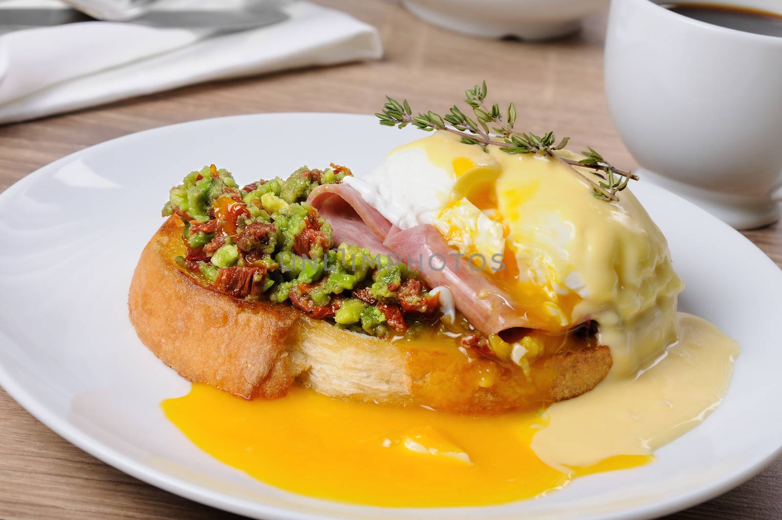 Toasted baguette slice with guacamole, ham and eggs Benedict under Dutch sauce