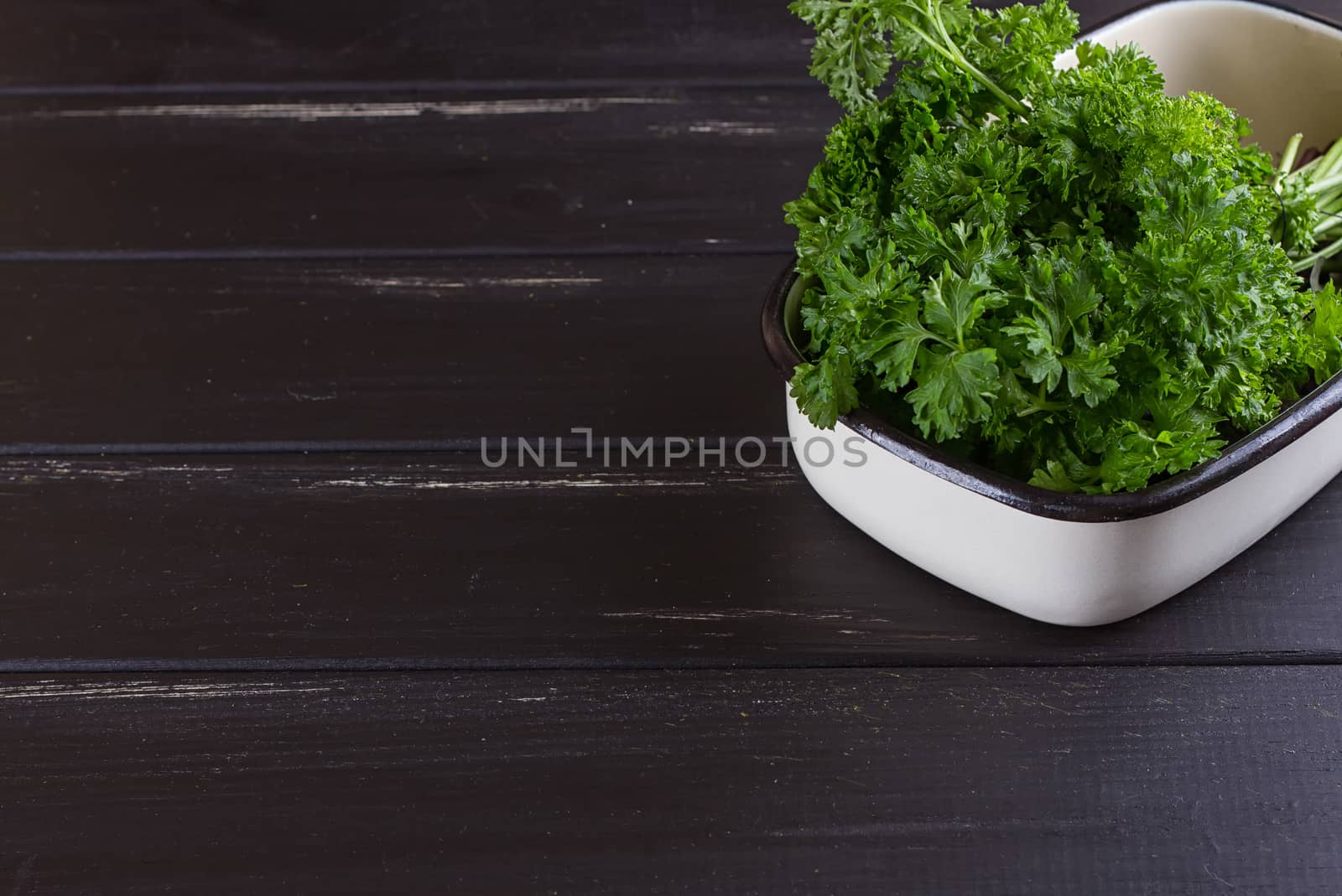 A bunch of fresh parsley in a ceramic tray on a black background. Fresh greens for salad