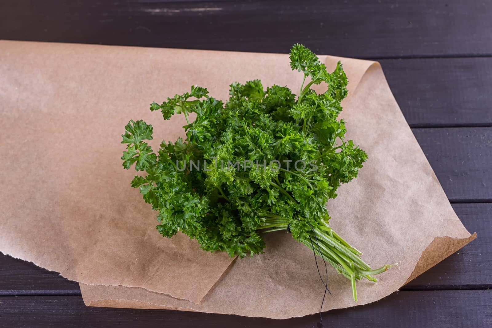 Bunch of parsley and wrapping paper on black wooden background. Copy-space composition
