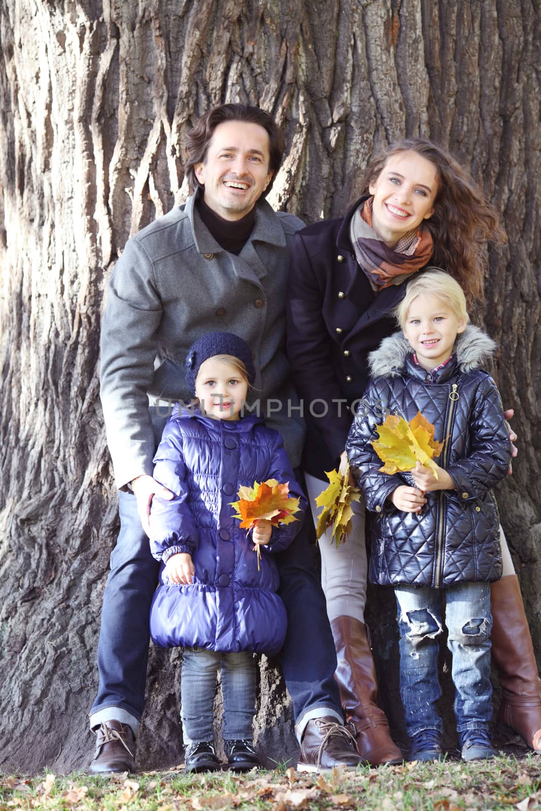 Happy family in autumn park near big tree trunk