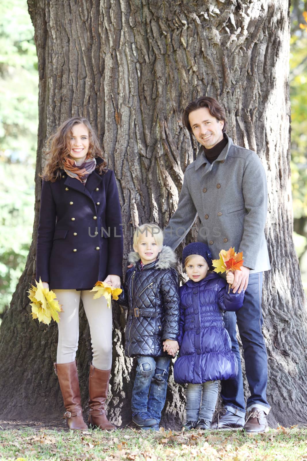 Happy family in autumn park near big tree trunk