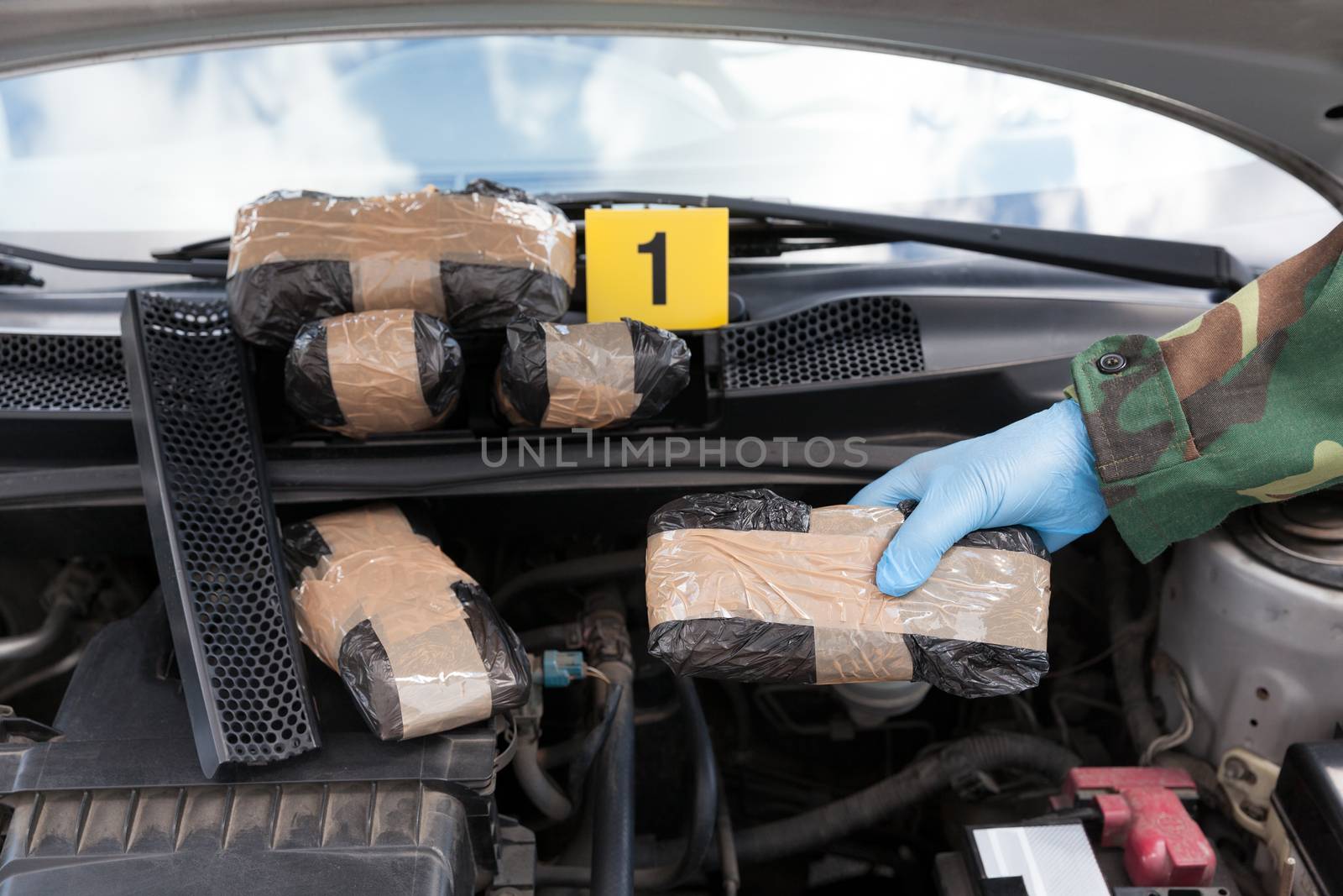 Policeman holding drug package found in engine compartment of a car