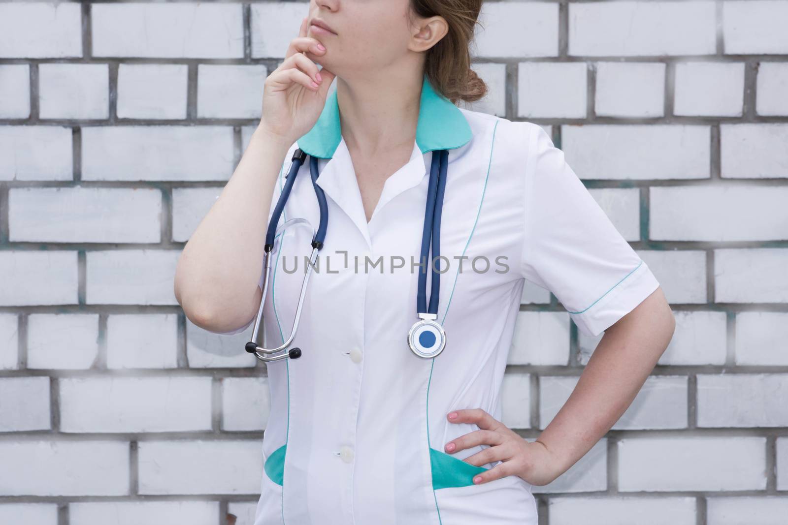 The doctor's concept. Girl in medical uniform with a stethoscope near a brick wall. Meditation. With a hand under his chin. Photo for your design