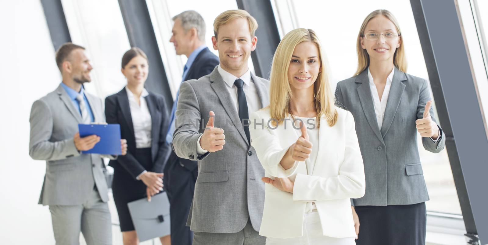 Confident business team showing thumbs up in office against the window