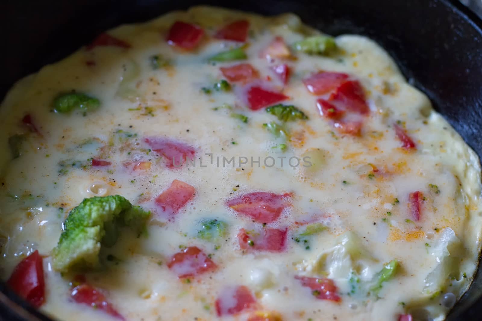 Cooking omelet in a pan, ready to serve. With tomatoes, red onion, goat's cheese and parsley