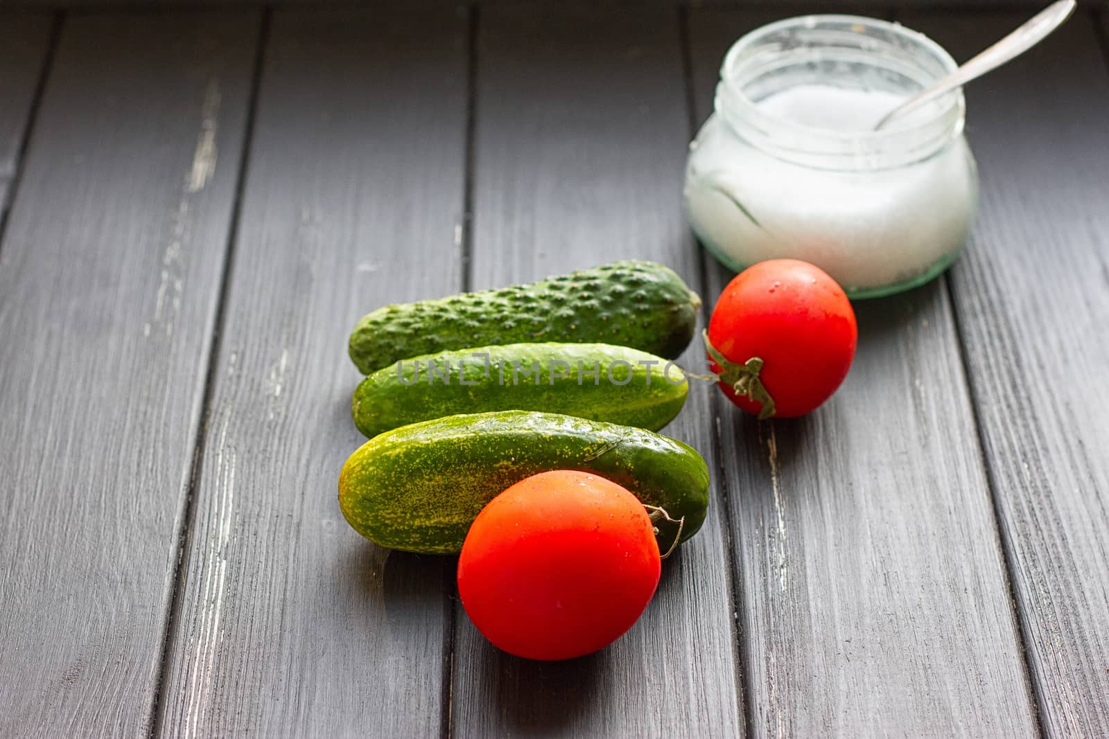 Tomatoes cucumbers and a can of salt on a black wooden background