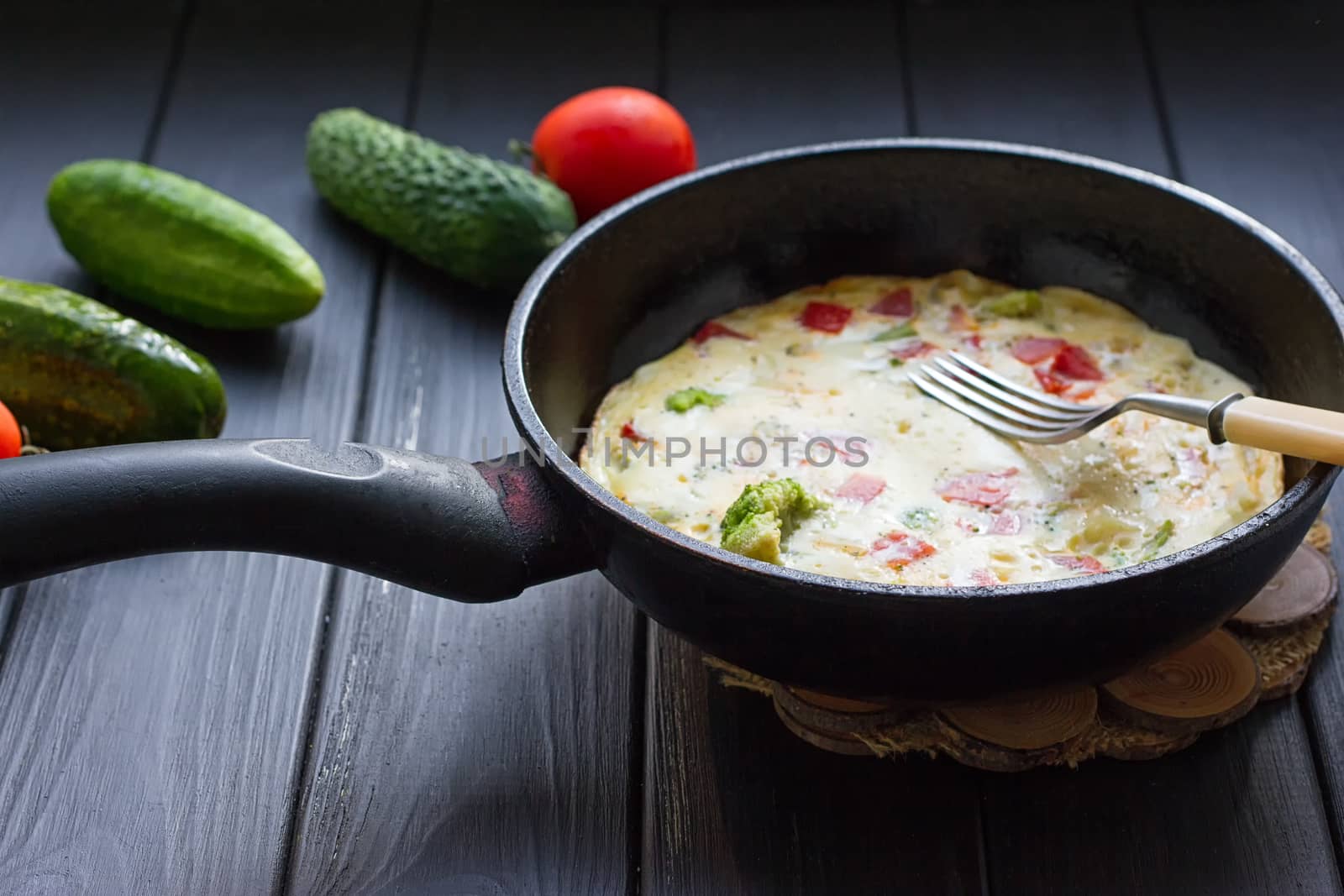 Breakfast set. Pan of fried eggs with fresh tomato, cucumber, sage on dark serving board over black background