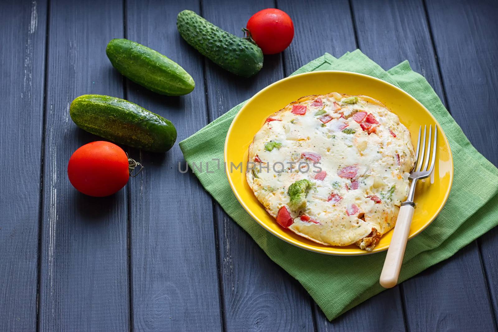 Hearty and tasty breakfast, traditional in the hotel, omelette from chicken eggs with cheese, fresh vegetables - cucumber and tomato on the black wooden background