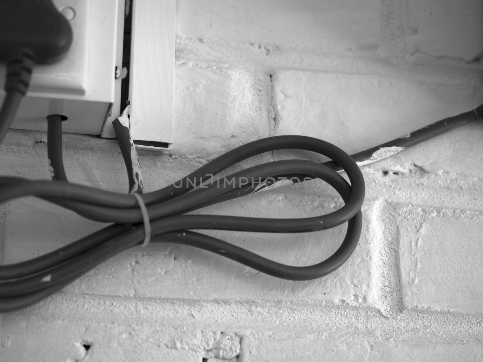 BLACK AND WHITE PHOTO OF ELECTRICAL CABLE ON WHITE BRICK WALL