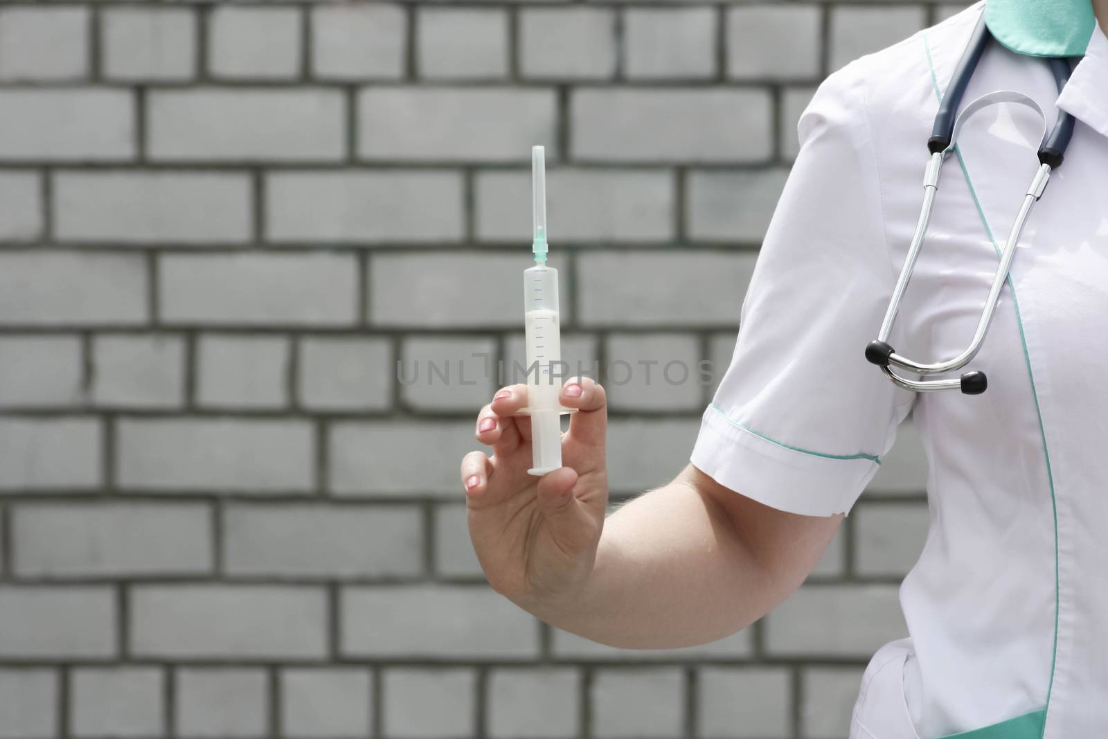 Medicine concept doctor. Injection. On a white brick wall background. Holds a syringe with a needle. Photo for your design