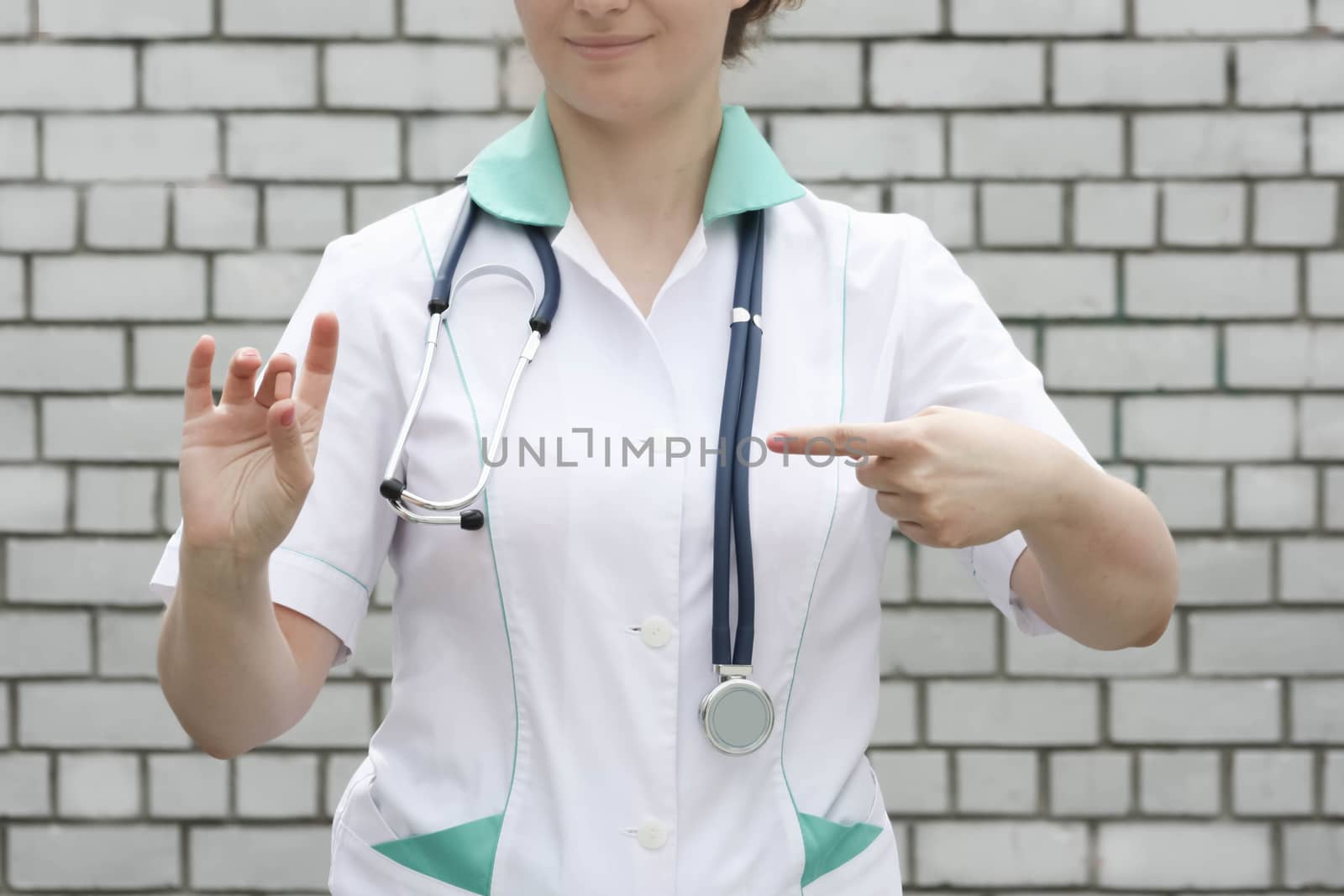 Medicine concept doctor. On a white brick wall background. Holds a pink pill. Advertising of products is indicated by a finger. Photo for your design