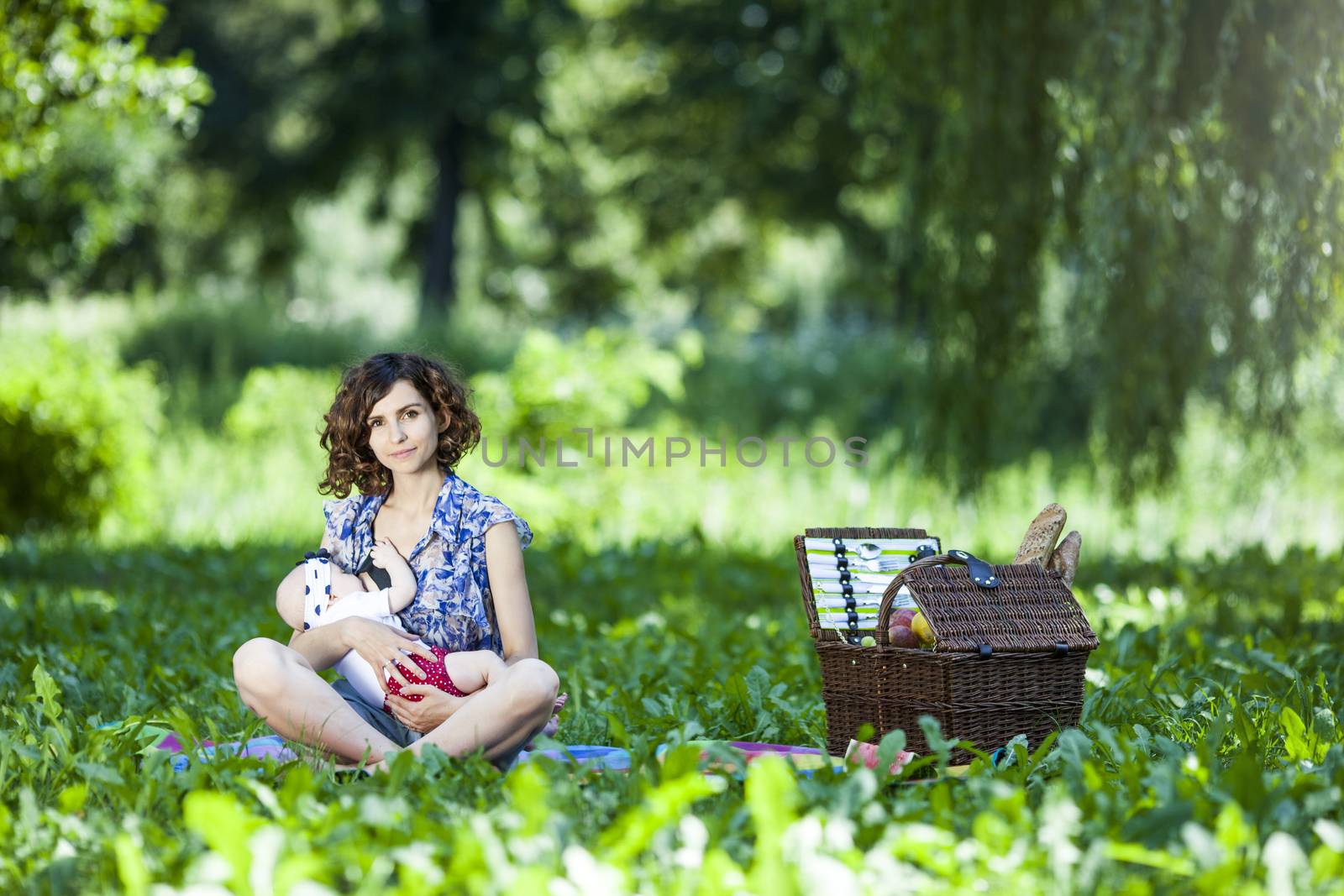 Young beautiful mother sits on blanket with her daughter during a picnic in the park