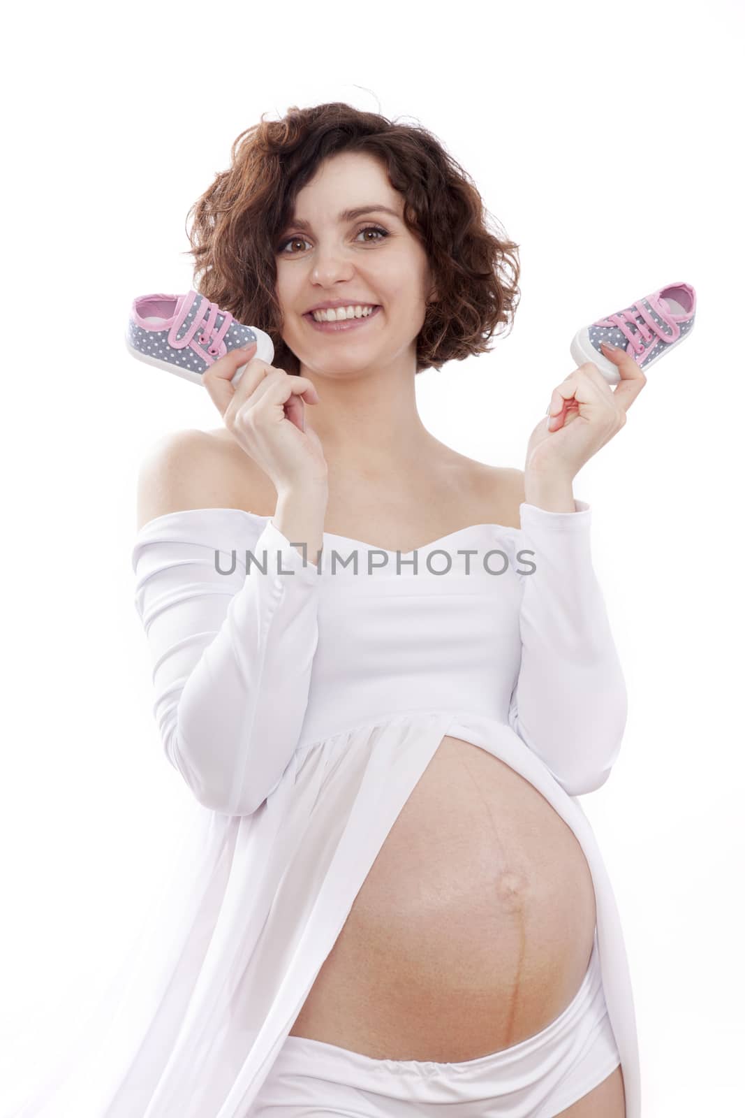 pregnant woman in a white dress holding a tiny baby shoes.