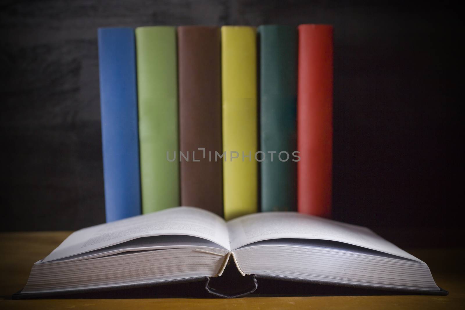 Open book and colorful books on a wooden table