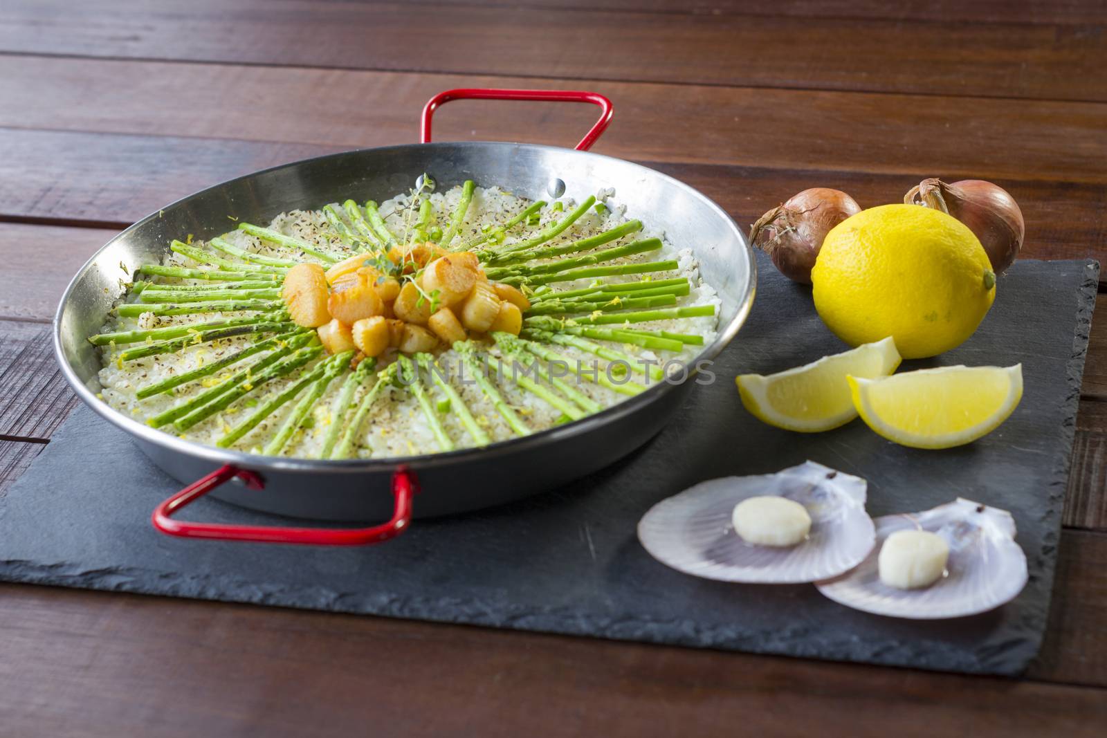 Paella with scollops and asparagus in traditional pan.