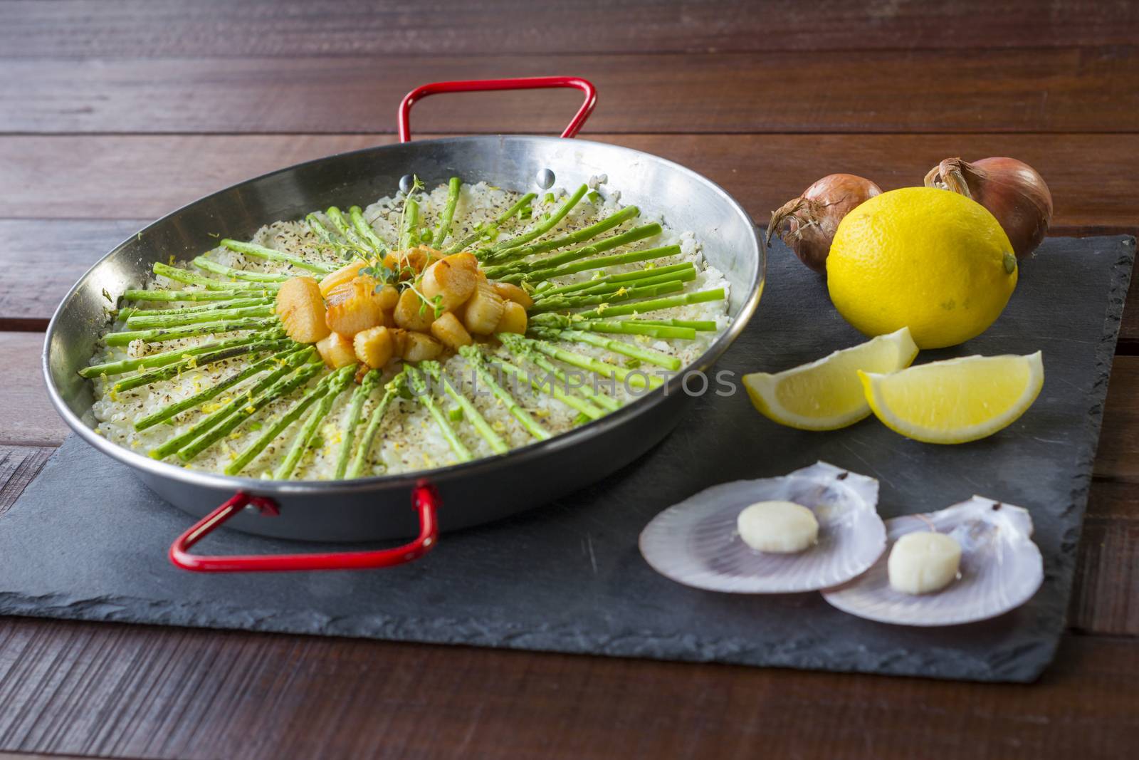 Paella with scollops and asparagus in traditional pan.