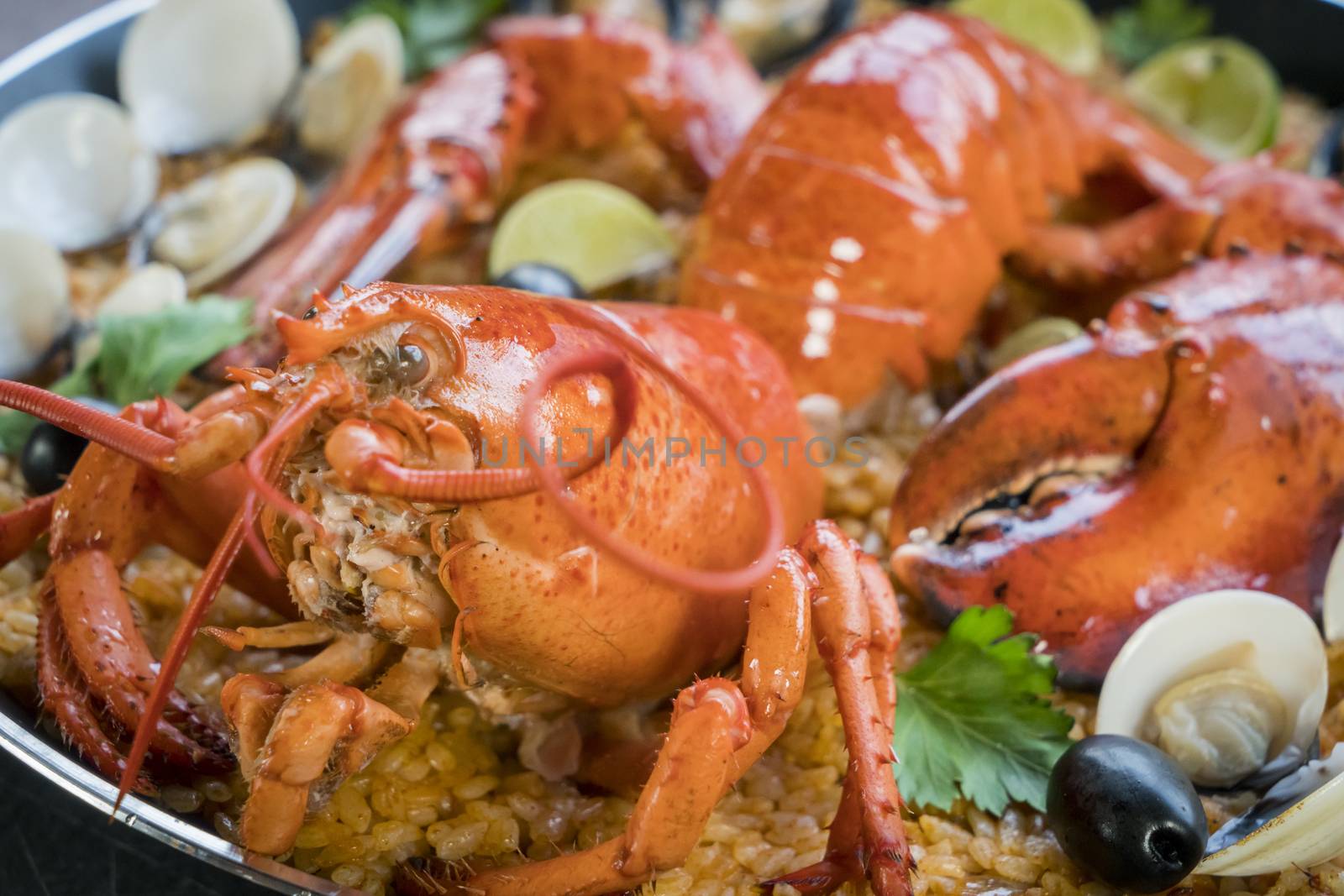 Gourmet seafood Valencia paella with fresh langoustine, clams, mussels and squid on savory saffron rice with peas and lemon slices, close up view