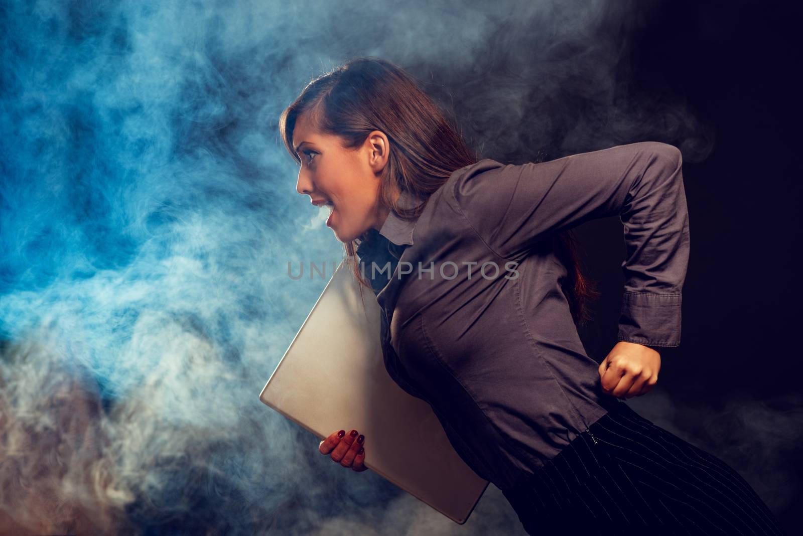 Stressed businesswoman running with laptop. Dark background.