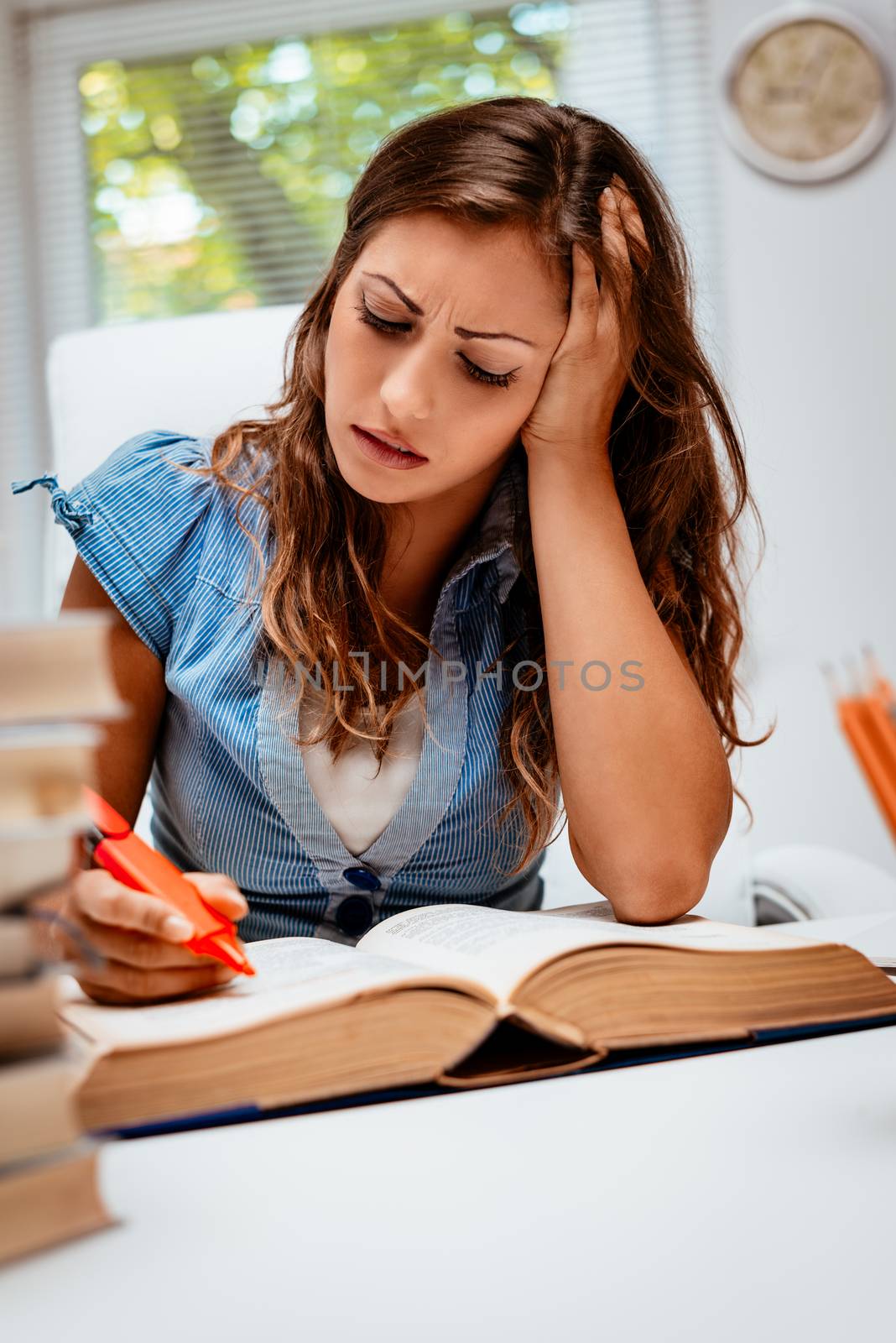 Beautiful young woman learning in the library. She is reading book and holding her head.