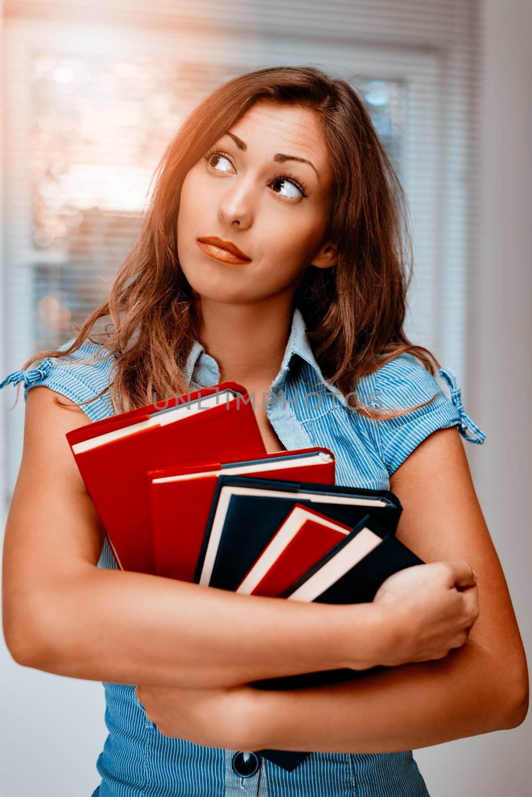 Beautiful teenage girl standing and holding colorful books.