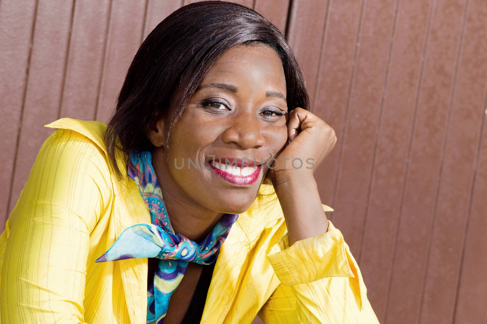 This young woman sitting hand under chin, smiling seems to be tired.