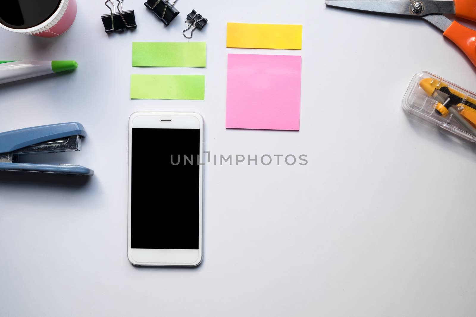 Top view of copy space of white working table work space with notebook, cup,note paper,pencil,clip,smartphone and other supplies.