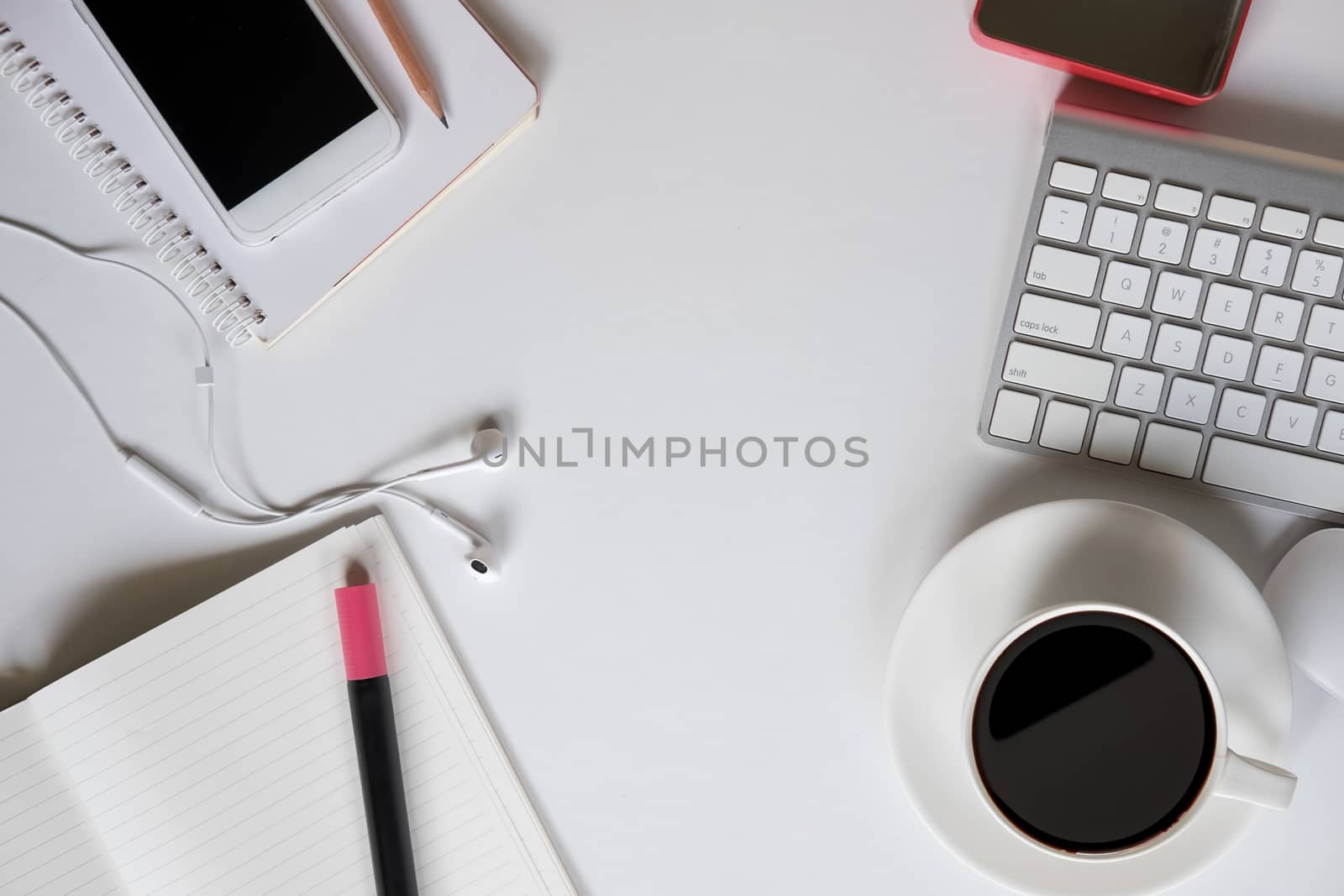 Top view with work space and copy space of white working table with keyboard, smartphone, cup of coffee and other supplies.
