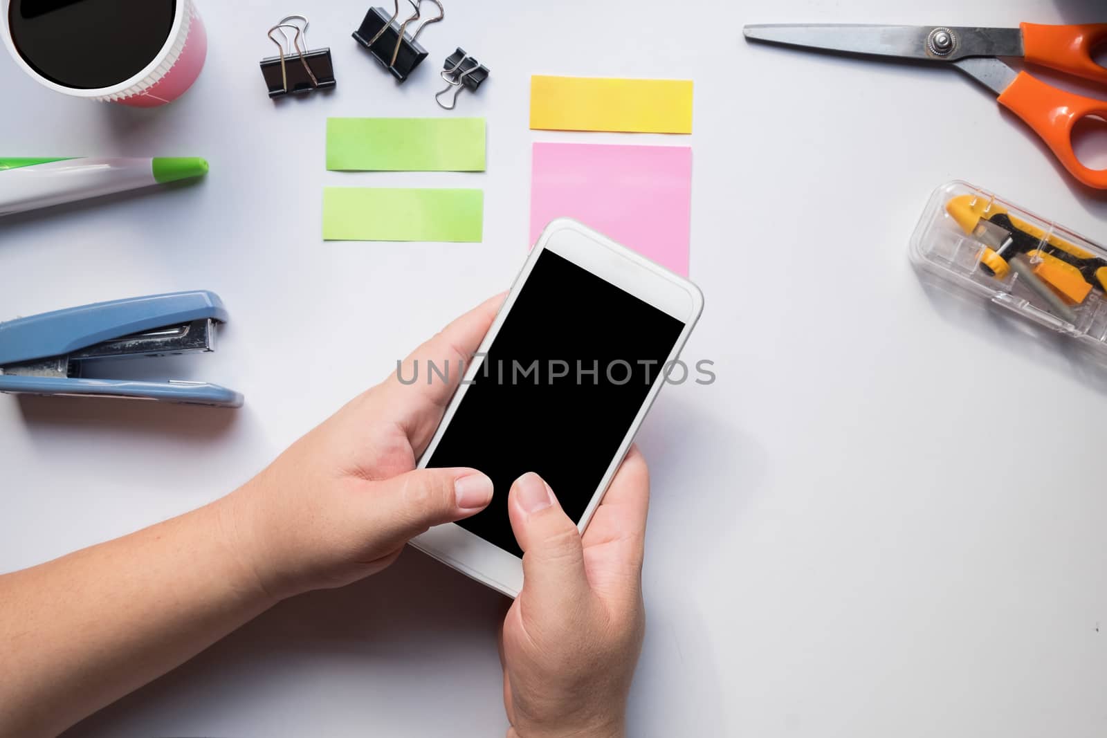 Hand using smartphone on office desk, workplace concept.