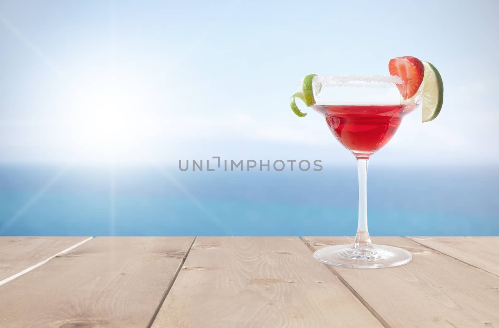 Red cocktail beverage with lime and ice by the coast