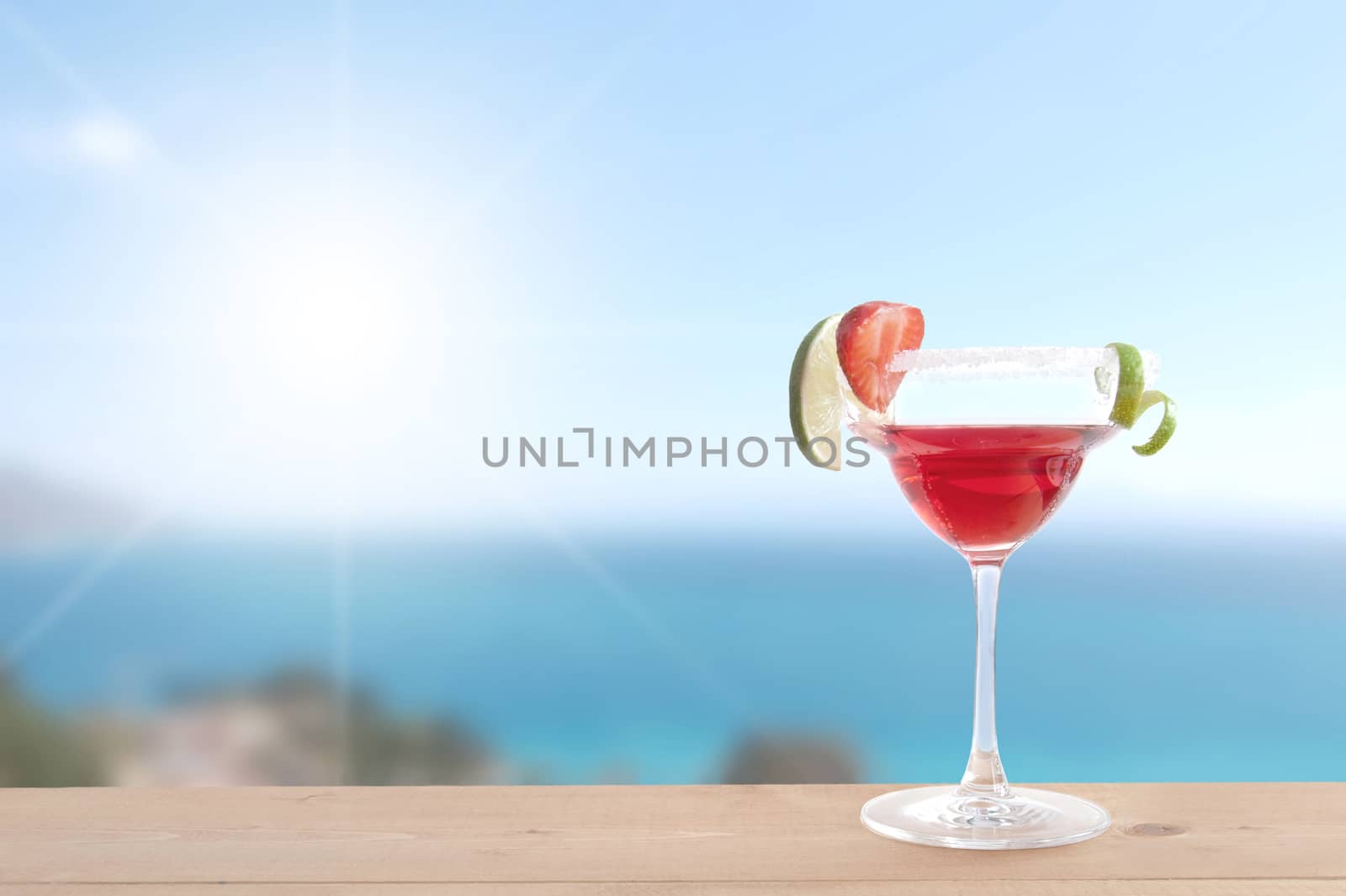 Red cocktail beverage with lime and ice by the coast