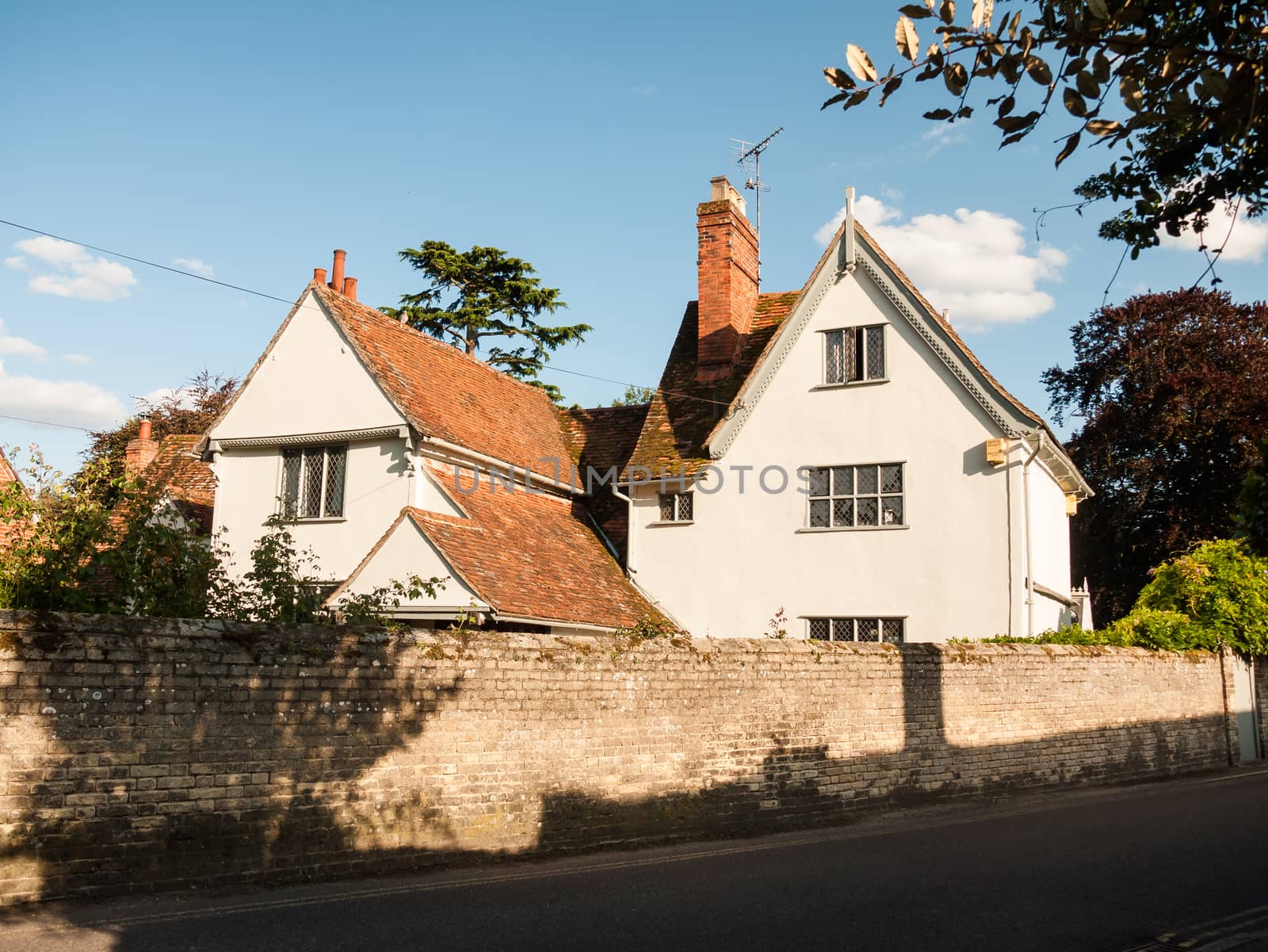 a white lovely cottage house in soft light and a brick wall and road in dedham; UK