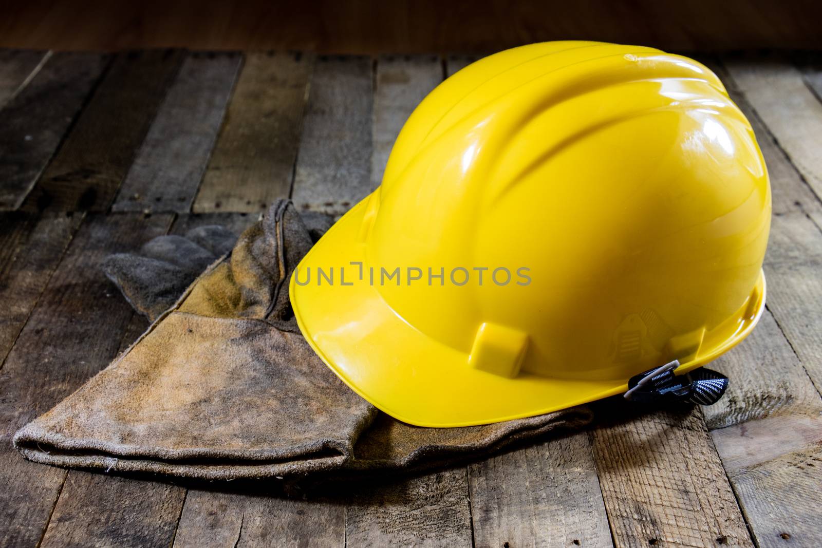 Yellow helmet and welding gloves. Black background and old wooden table.