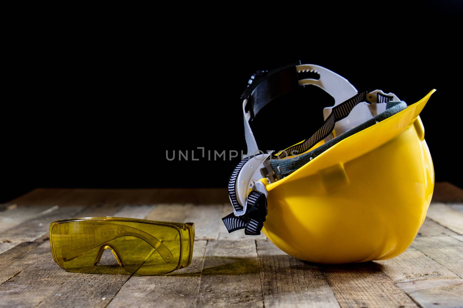 Yellow helmet and welding gloves. Black background and old wooden table.