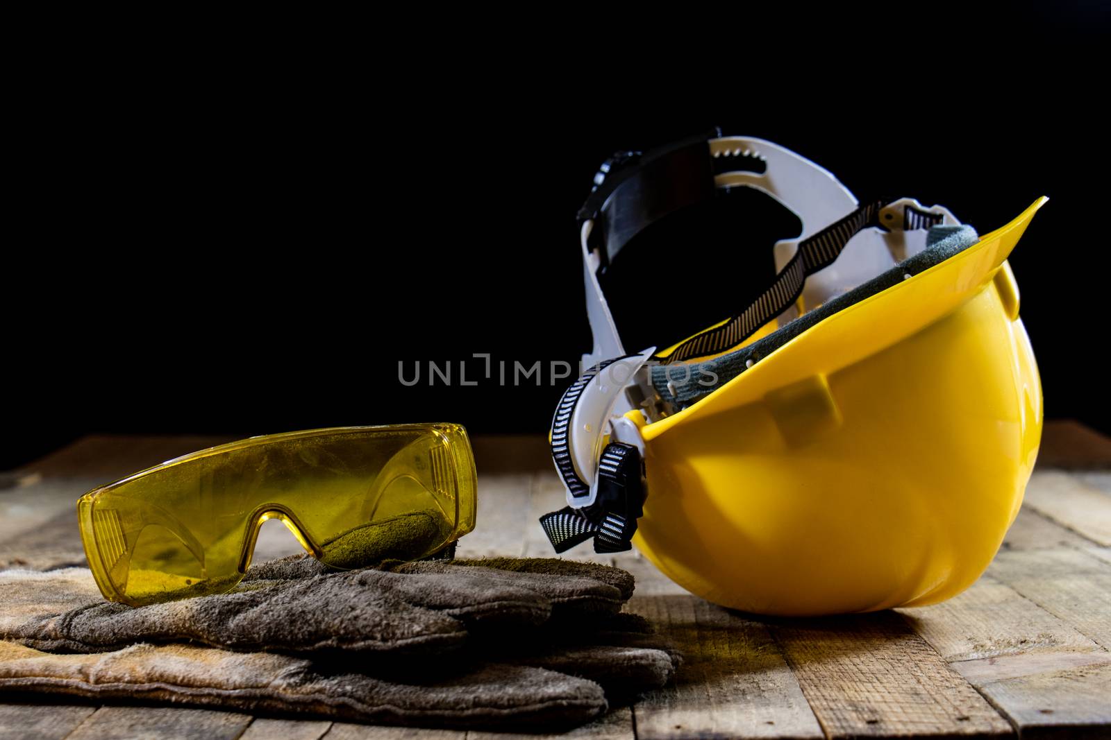 Yellow helmet and welding gloves. Black background and old wooden table.