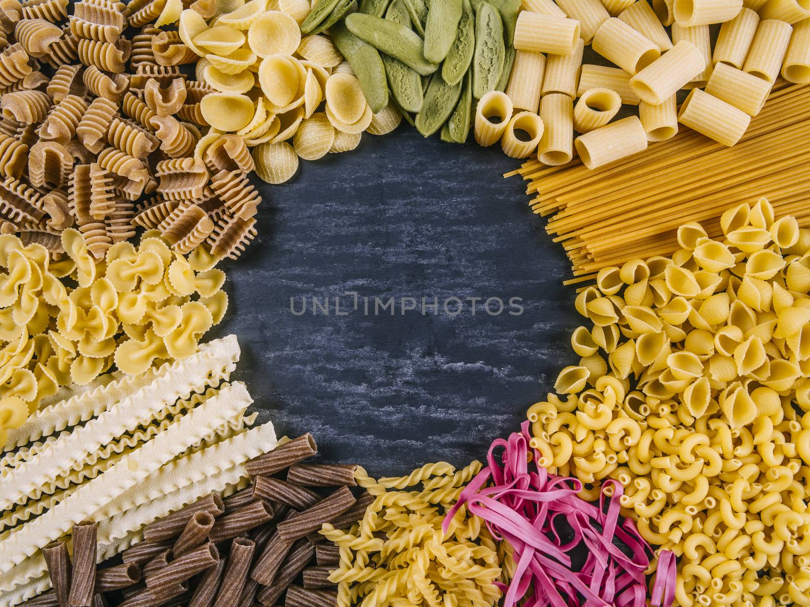 Photo of twelve different pasta types arranged on a slate surface as a frame.
