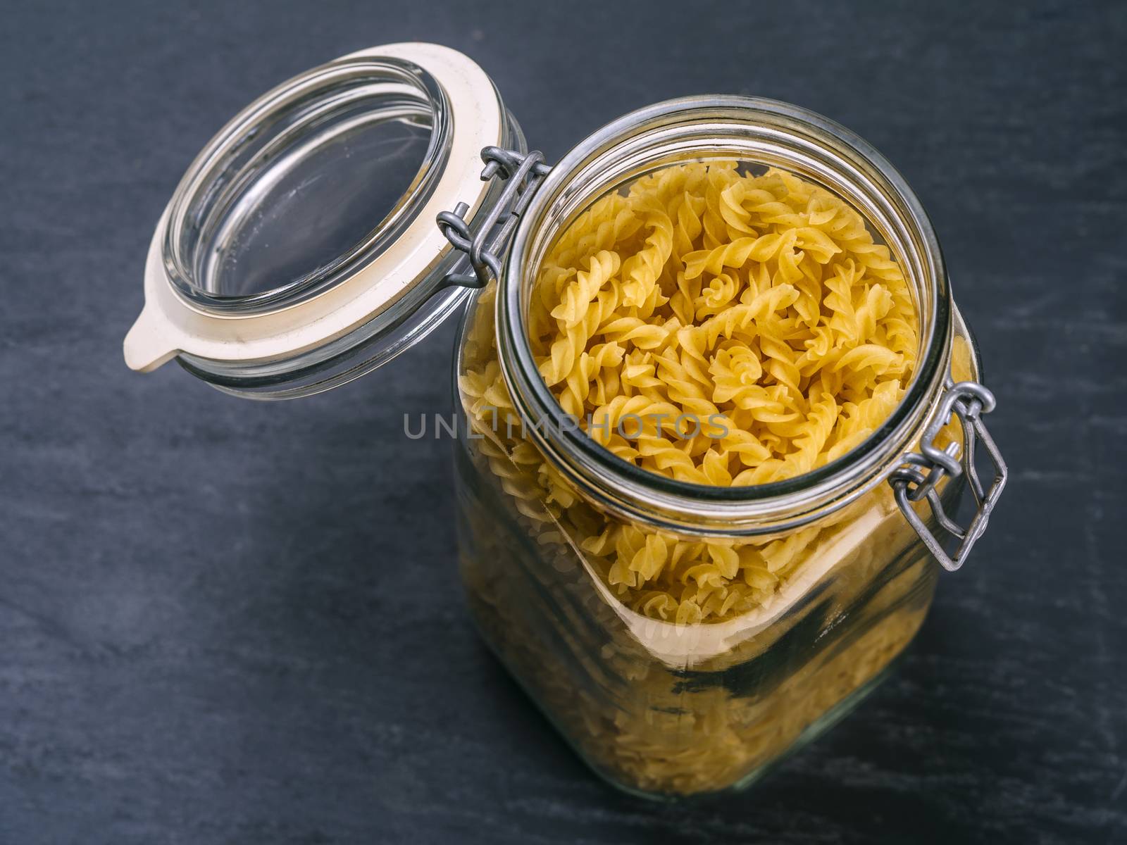 Photo of fusilli pasta in an open jar on top of a slate background.