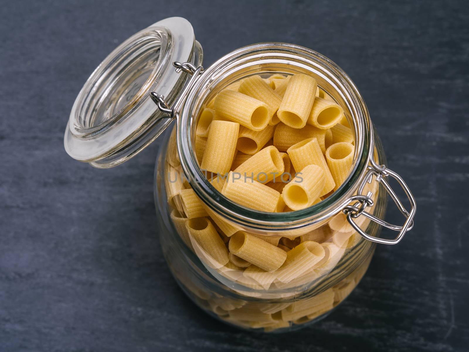 Photo of Mezzi Rigatoni in an open jar on top of a slate background.