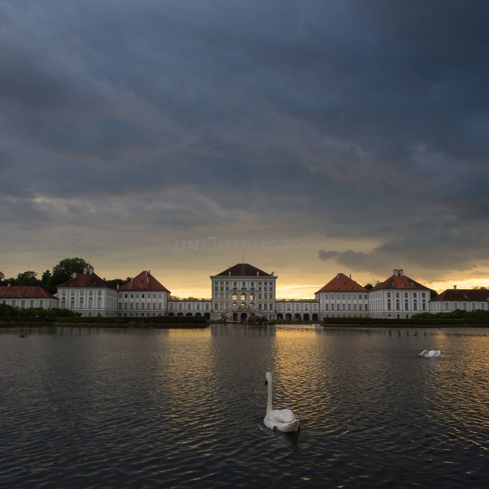 Dramatic scenery of Nymphenburg palace in Munich Germany. Sunset after the sorm. White swans and duks swimming in pond in front of the palace.