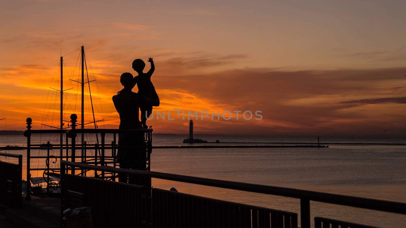 Silhouettes of mother and child against the background of the rising sun in the seaport