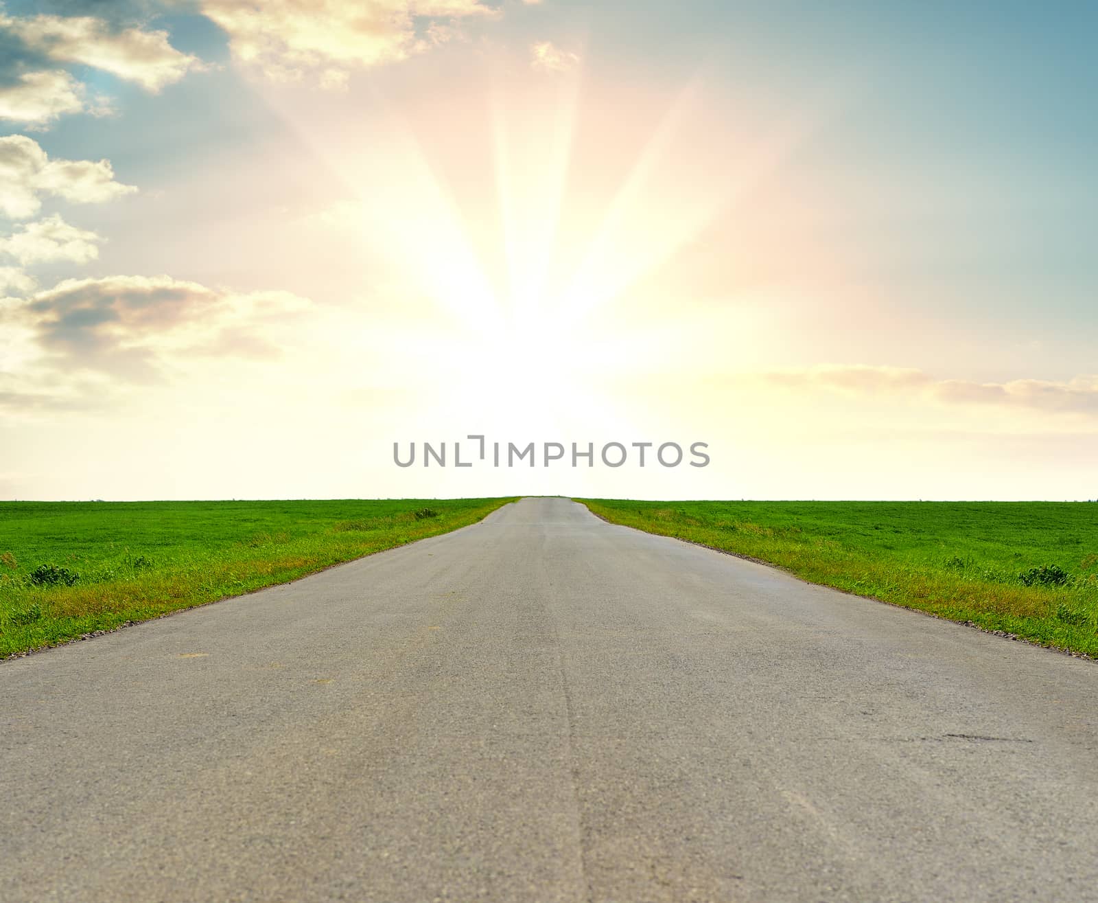Asphalt road in a grass field against a beautiful sunrise. The concept of success