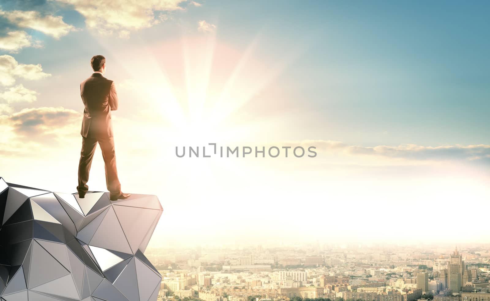 A businessman in a suit stands on an abstract metal construction and looks at the sunrise. Ahead of city landscape