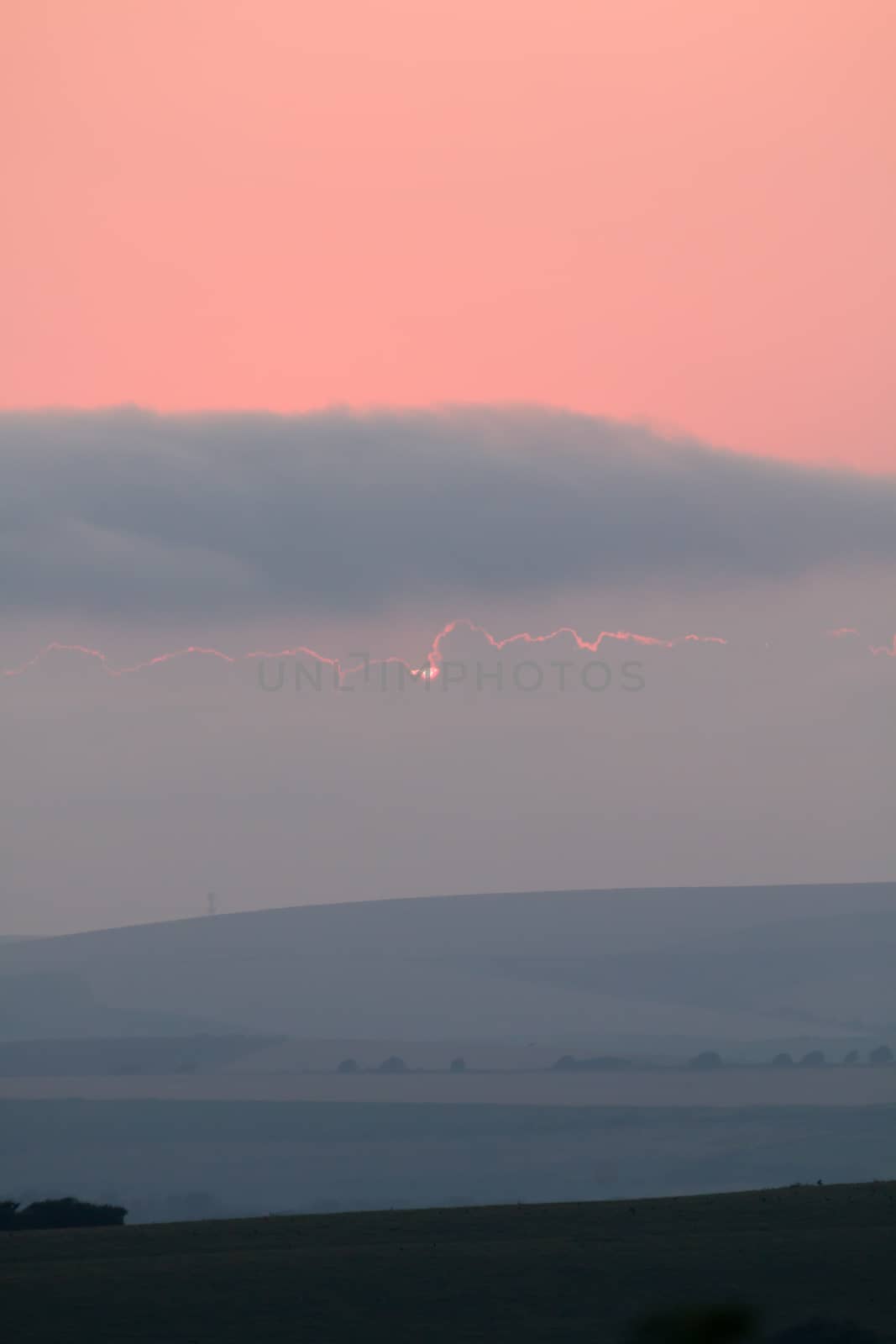 Sun just about to disappear behind cloud at sunset from Seaford, East Sussex looking across towards Beddingham Hill.