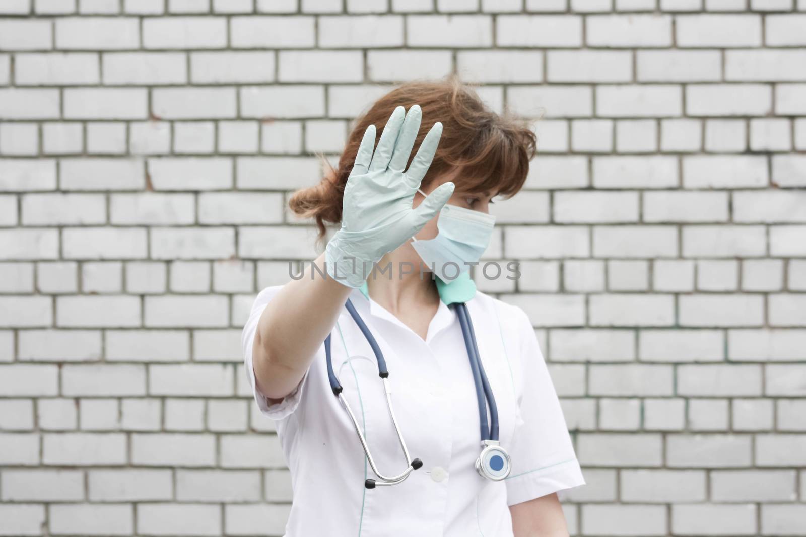 Doctor concept. Bad result of the operation. Girl in white medical dressing gown on brick wall background. Closes his face in the mask with his hand. Photo for your design. Horizontal sheet orientation