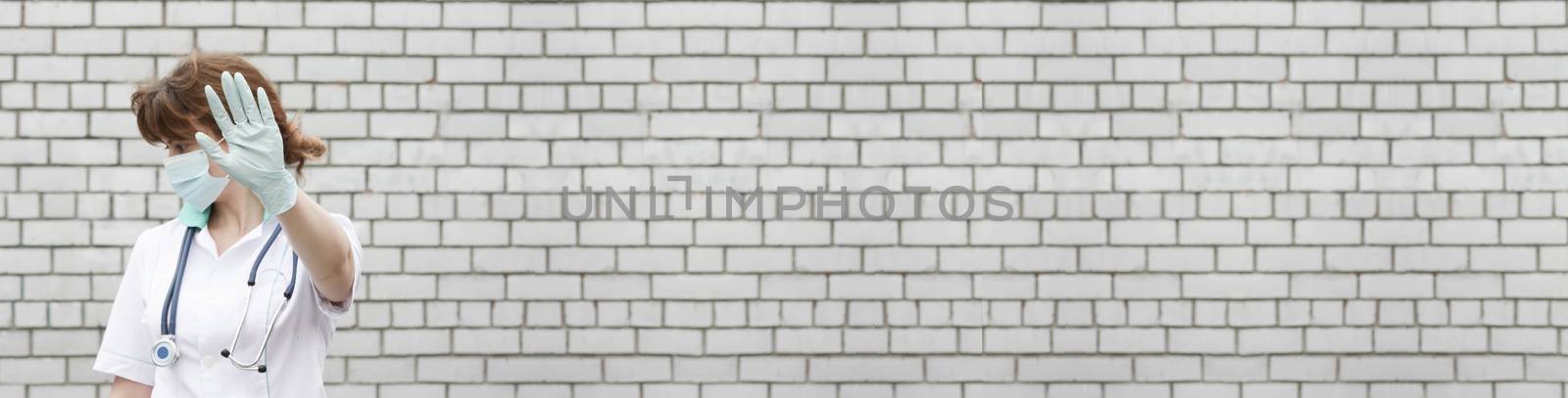 Doctor concept. Close your face with your hands. Medical error. Girl in white medical dressing gown on brick wall background. Photo for your design. Horizontal sheet orientation