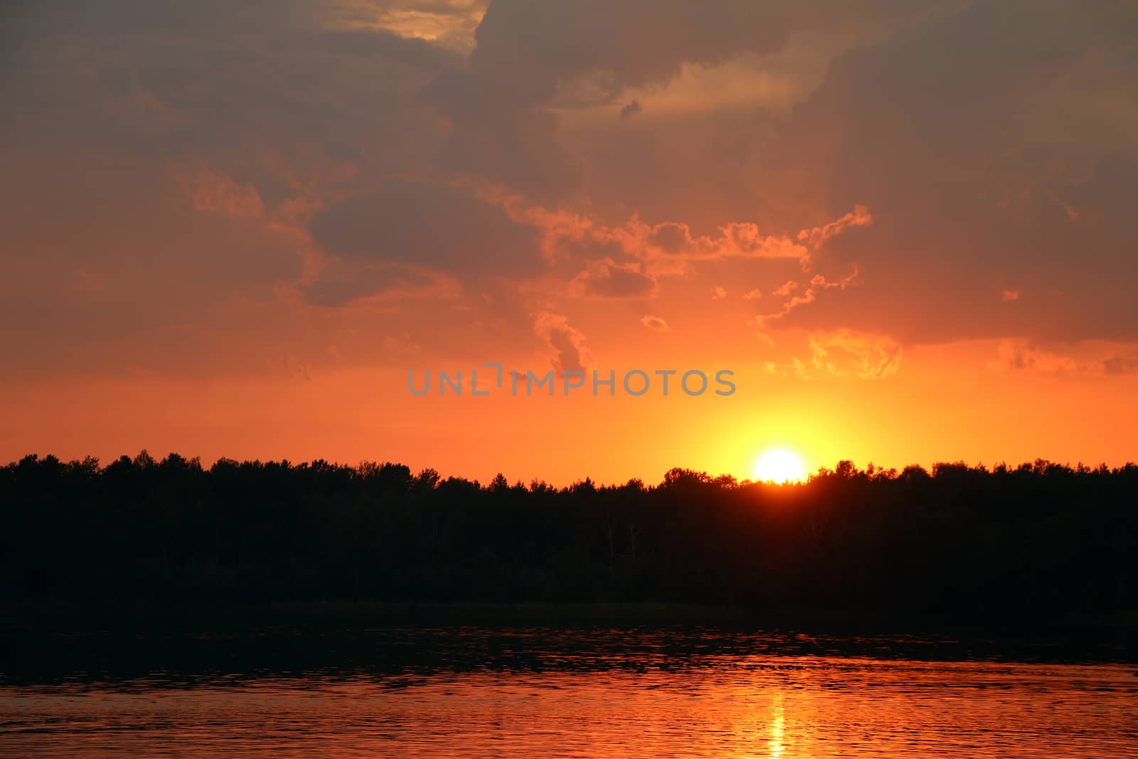 Storm clouds and sunset on lake and forest silhouette background. Nature summer sunlight wallpaper