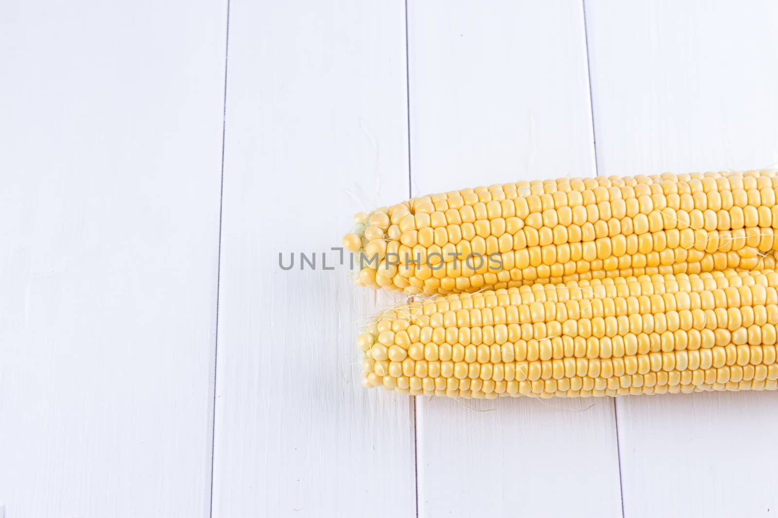 Two raw maize cobs at white wooden table background