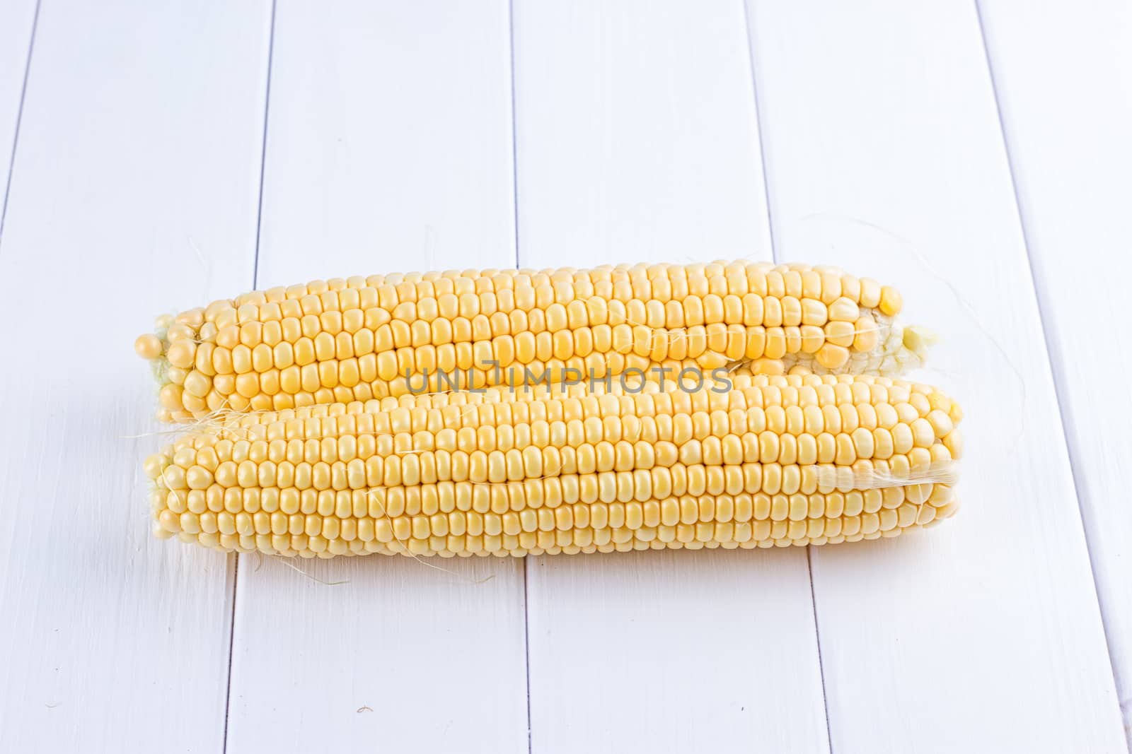 Two raw maize cobs at white wooden table background